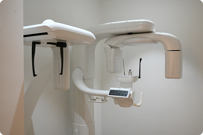 A sleek, modern panoramic dental X-ray machine in a clinical white room. It features multiple adjustable arms and a digital control panel, evoking a sterile, professional atmosphere.